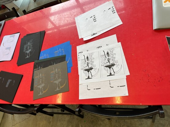 On the red desk of studio, there are hard copy of illustration and test prints
